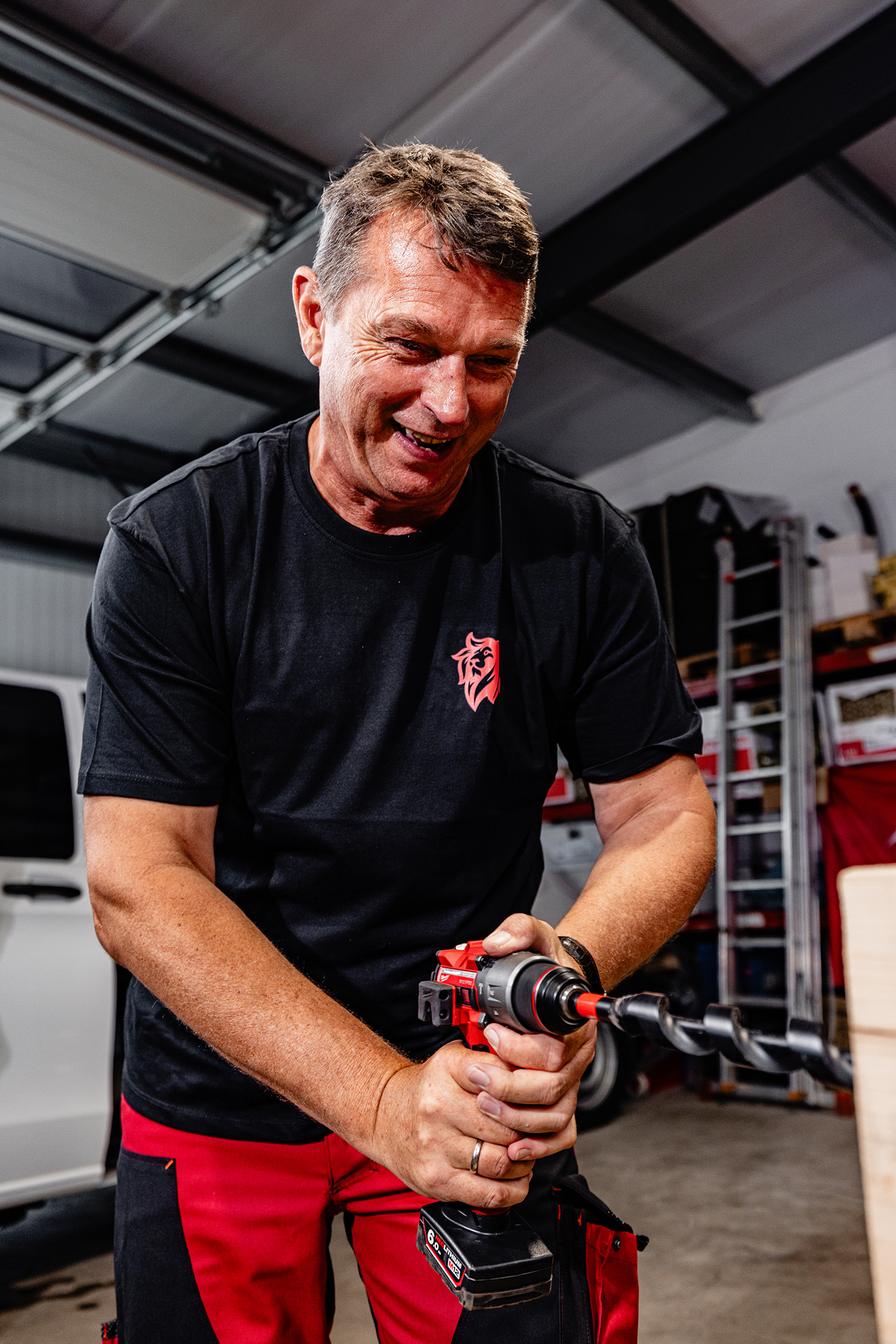 Handwerker in schwarzem T-Shirt mit rotem Logo präsentiert ein Elektrowerkzeug in einer Werkstatt der Roten Löwen GmbH.