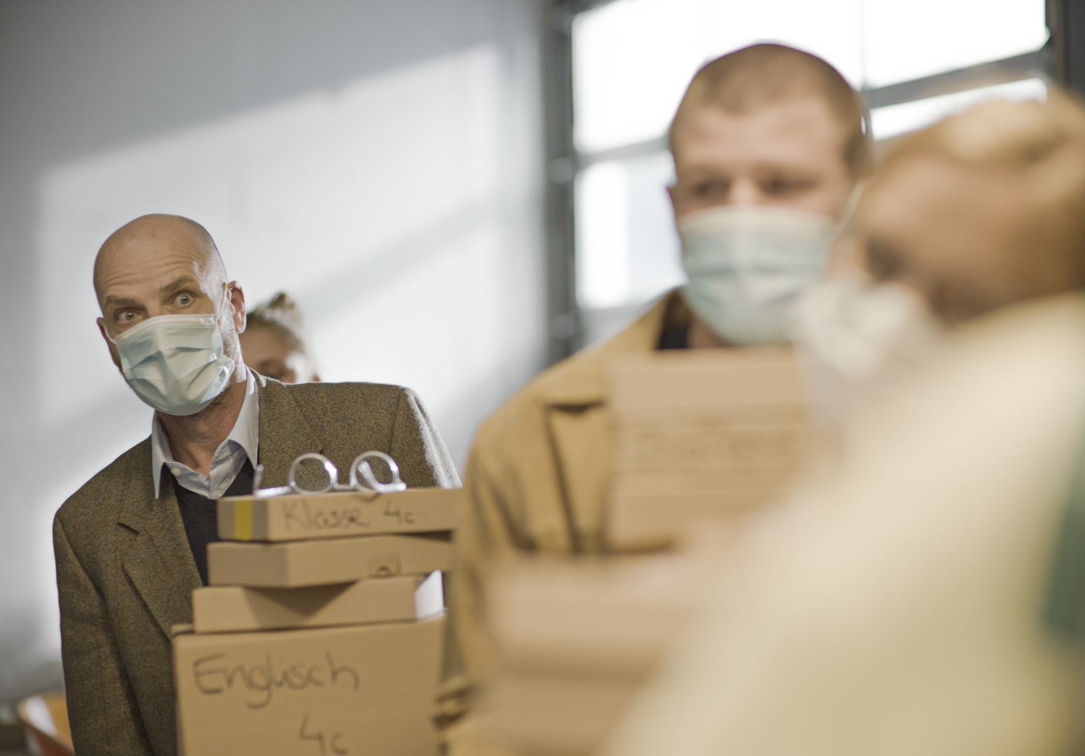 Mann mit Gesichtsmaske trägt Stapel Kartons in Büro, Kampagne in45Minuten der IServ GmbH