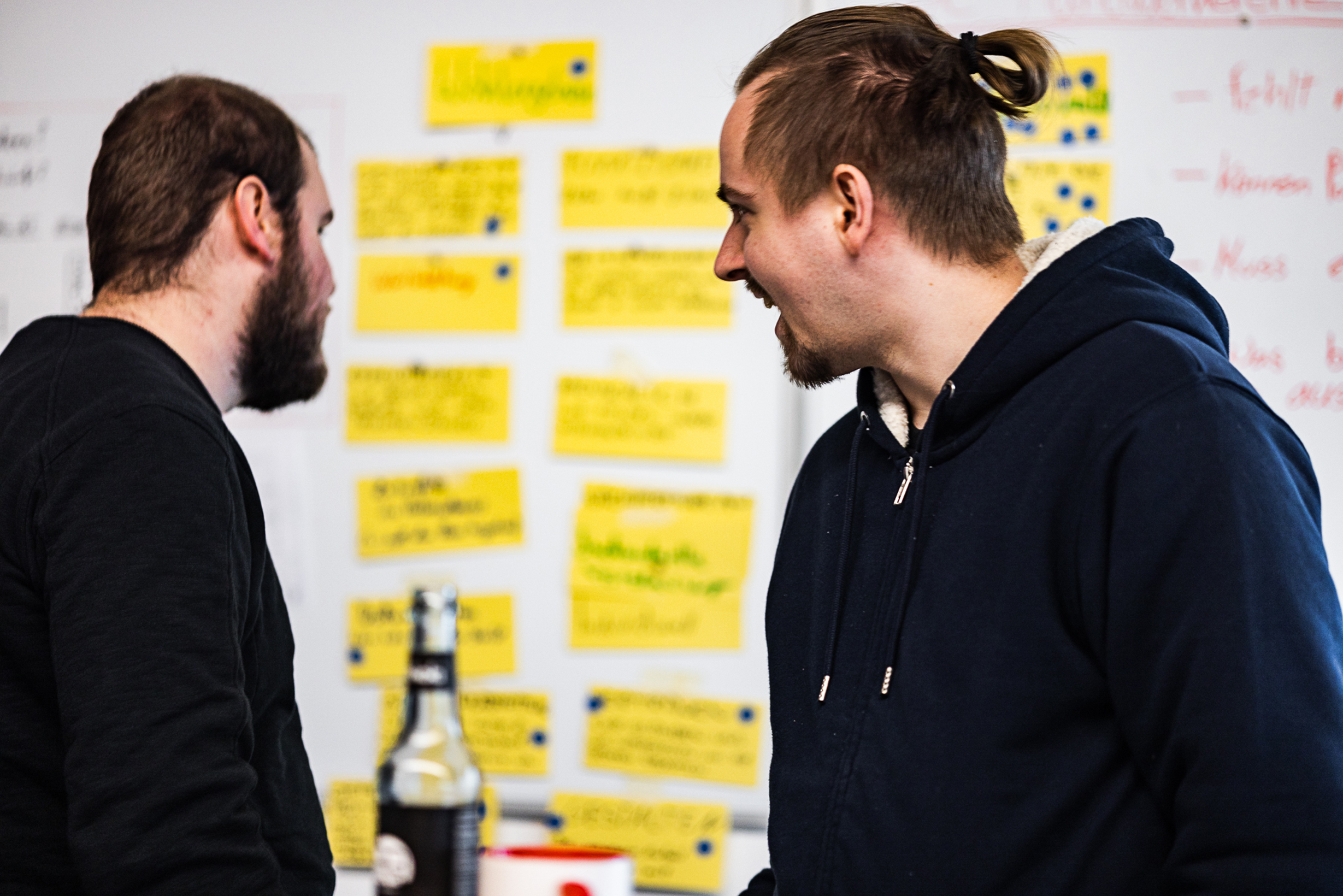 Zwei Männer diskutieren vor einer Pinnwand mit gelben Notizzetteln während eines Brainstorming- oder Planungsworkshops zur Kultur- und Markenentwicklung.