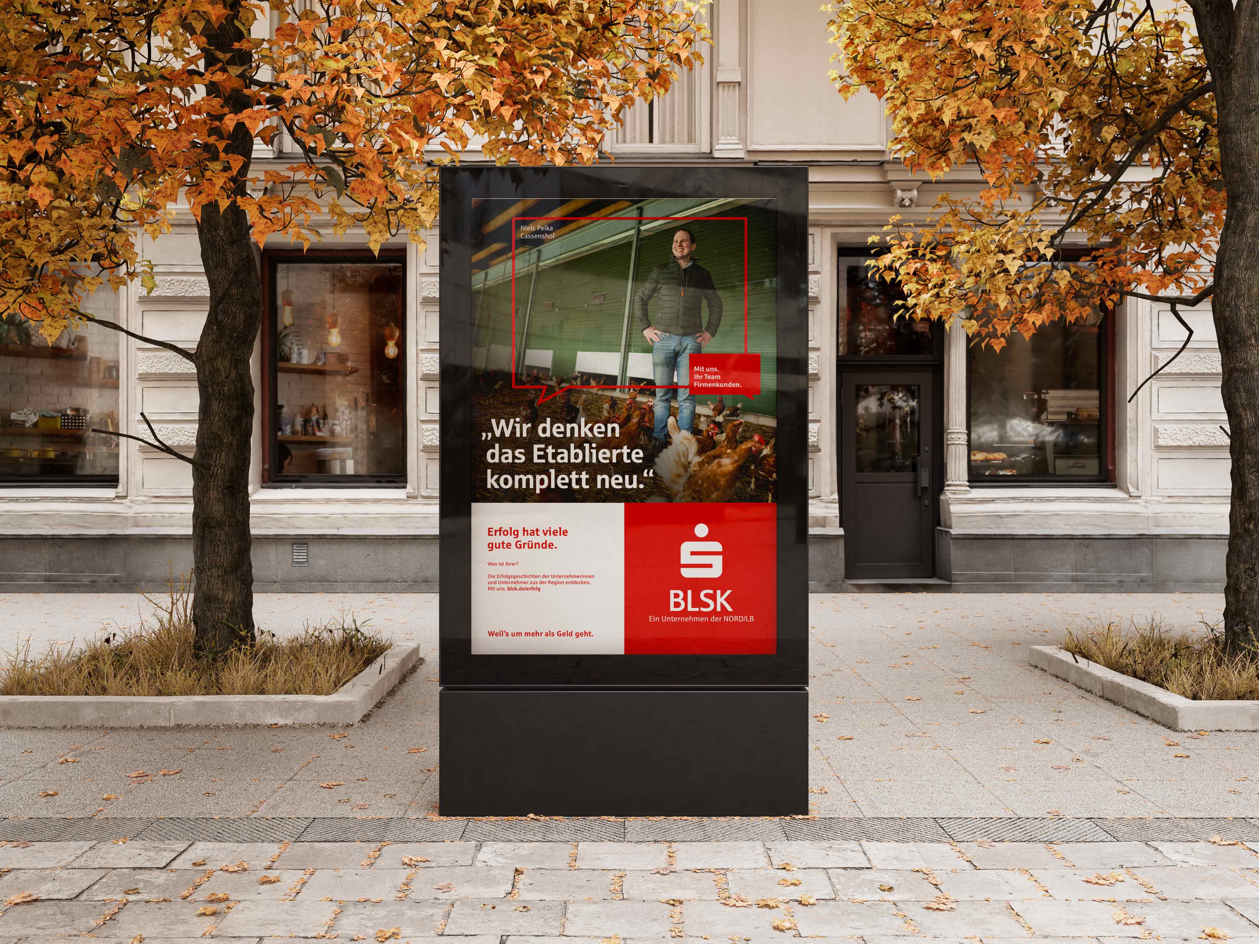Digitale Außenwerbung der Braunschweigischen Landessparkasse mit Kampagnenmotiv zur Renovierung eines Etablissements, umgeben von herbstlichen Bäumen vor klassizistischem Gebäude