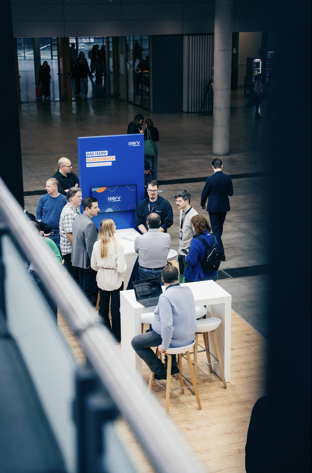 Event-Stand der IServ Gruppe mit blauem Ausstellungsmodul in moderner Halle, Besucher informieren sich an Stehtischen über Markenentwicklung und Dienstleistungen.