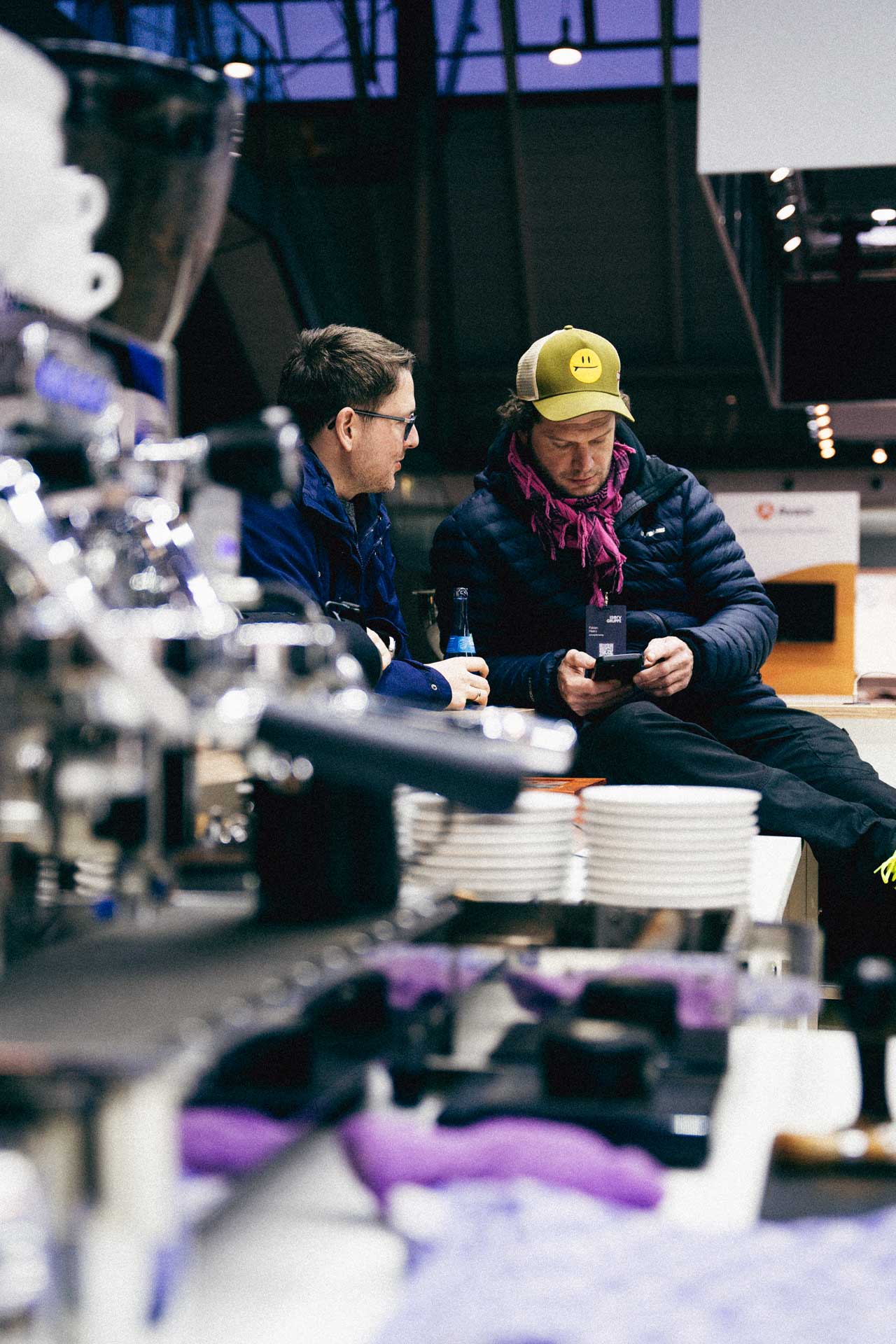 Zwei Personen diskutieren an einem Tisch während einer IServ-Veranstaltung mit Robotik-Ausstellung in einer modernen Industriehalle.